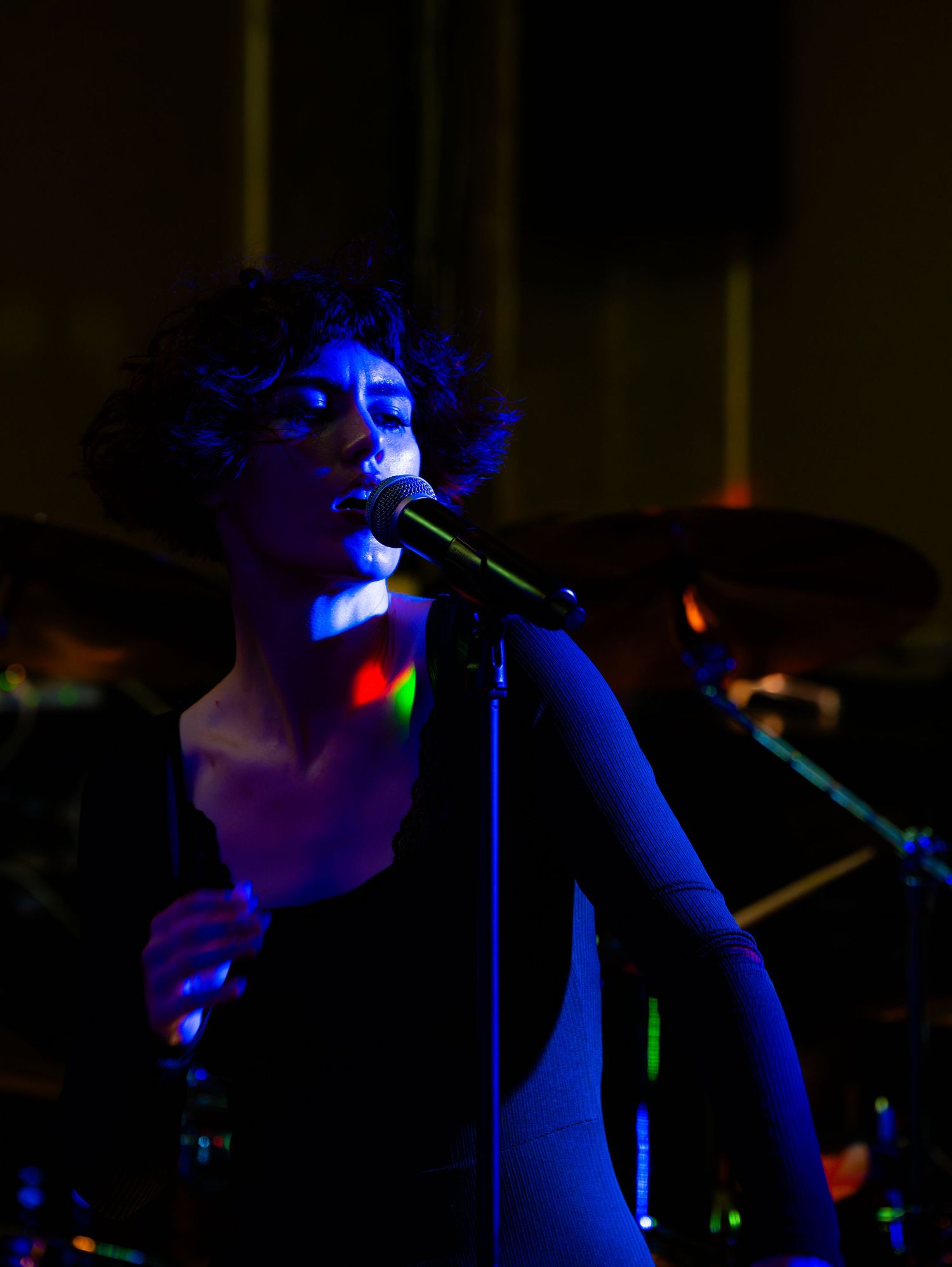 Singer performing on a dimly lit stage with blue lighting effects creating a moody atmosphere.