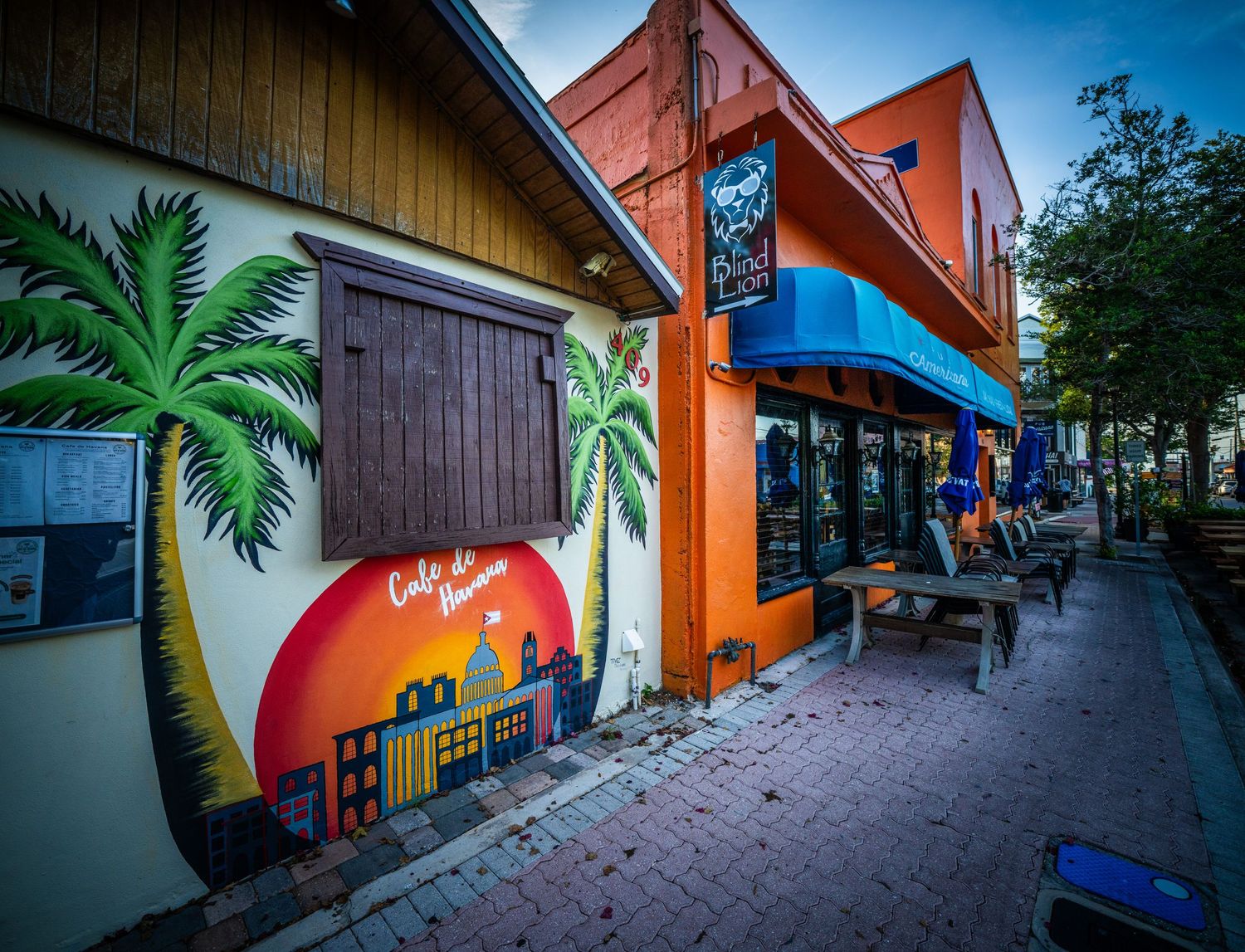 Vibrant orange building exterior with tropical palm tree murals and outdoor seating area.