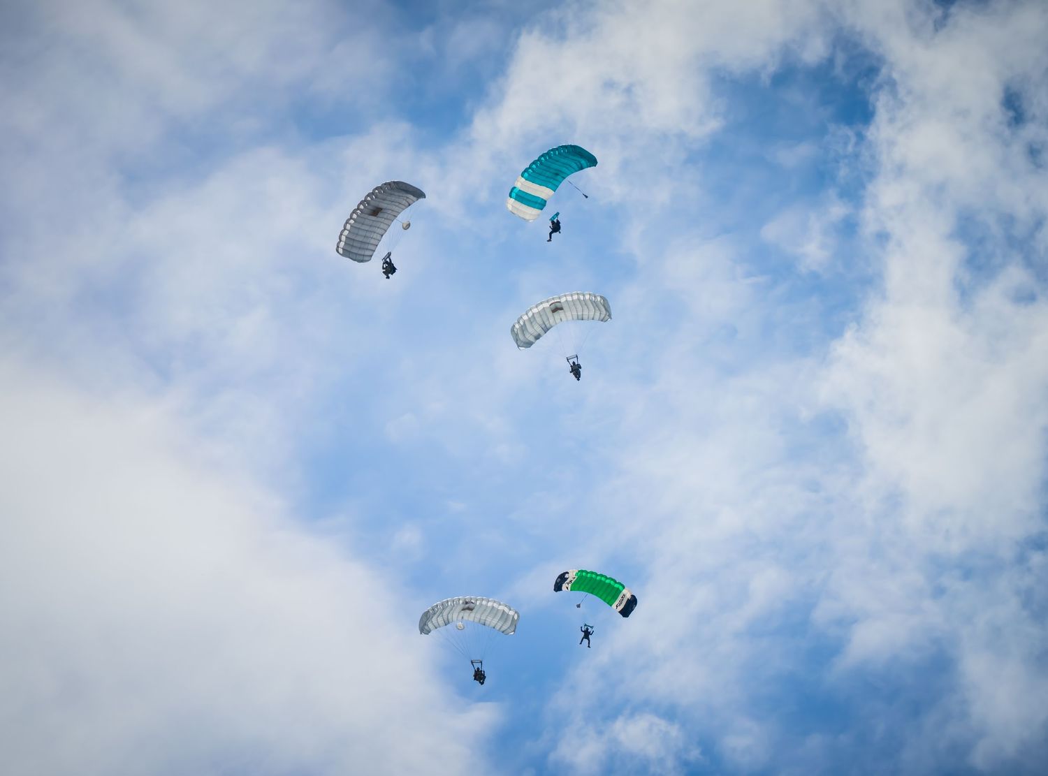 Formation of parachutes in green and white colors floating against a bright blue sky.
