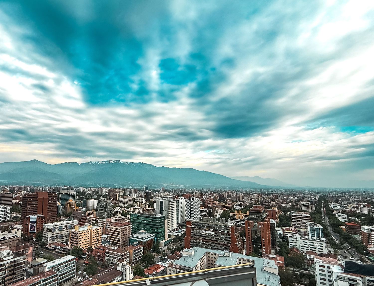 Urban skyline of Santiago Chile with dramatic cloudy sky and mountain backdrop.