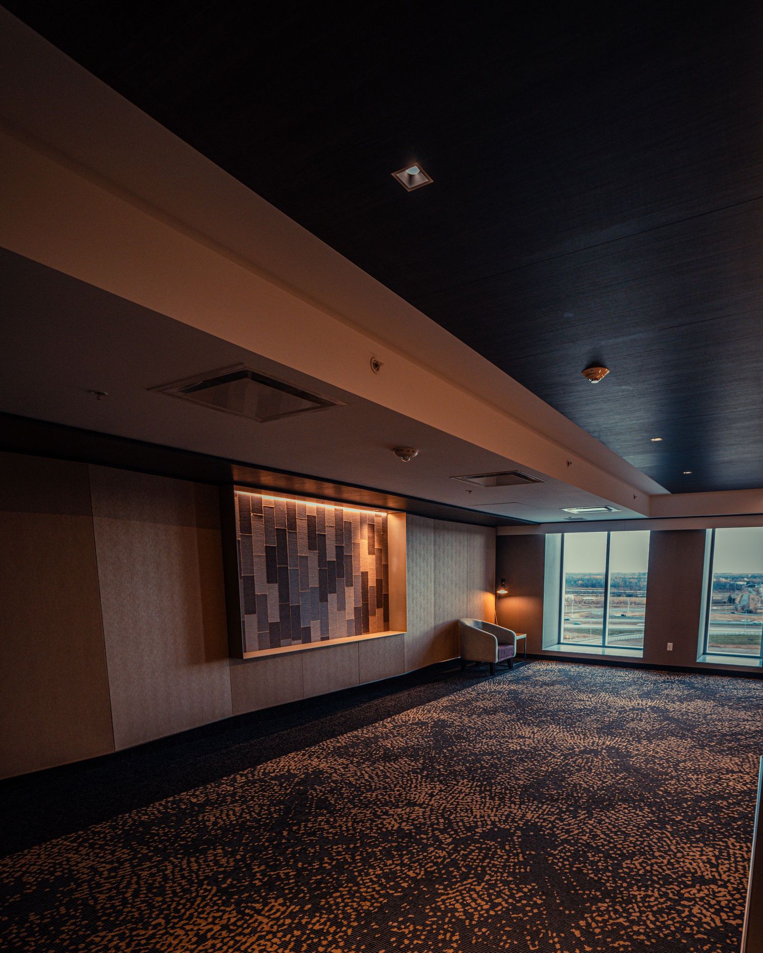 Long dark hallway with patterned carpet and modern wall lighting fixtures.