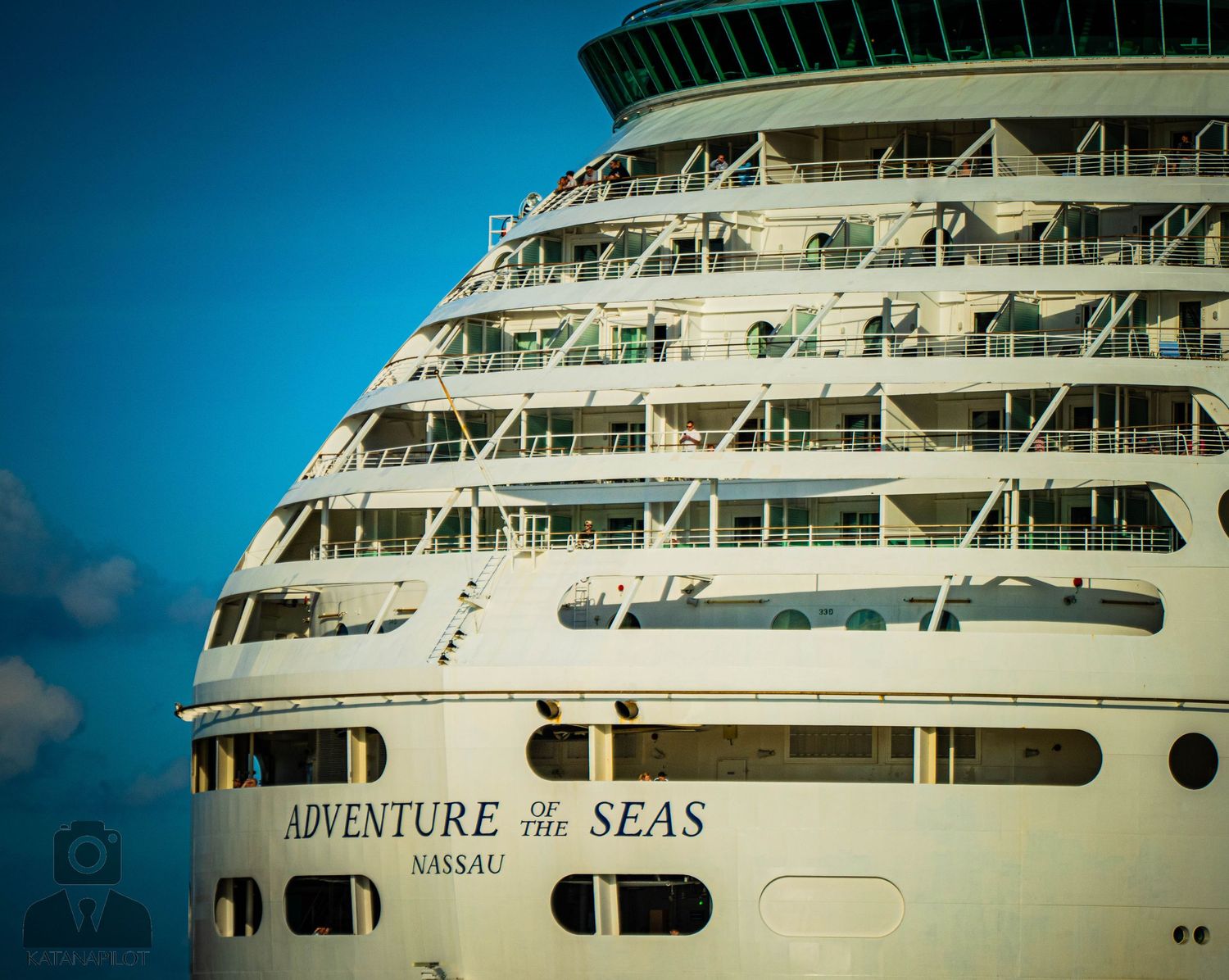 Side view of a large white cruise ship named Adventure of the Seas against a blue sky.