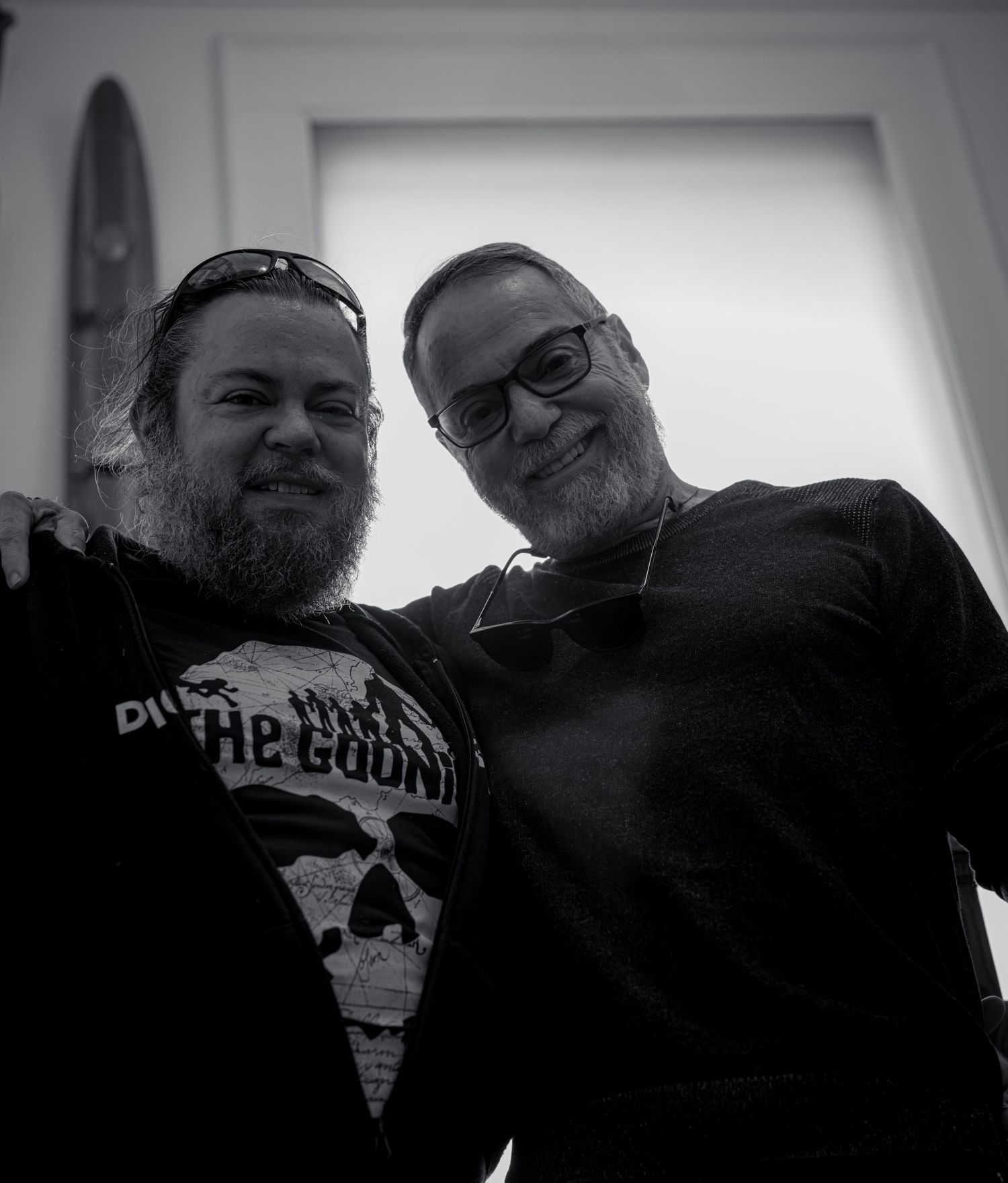 A black and white portrait of two men with beards wearing dark clothing against a light background.