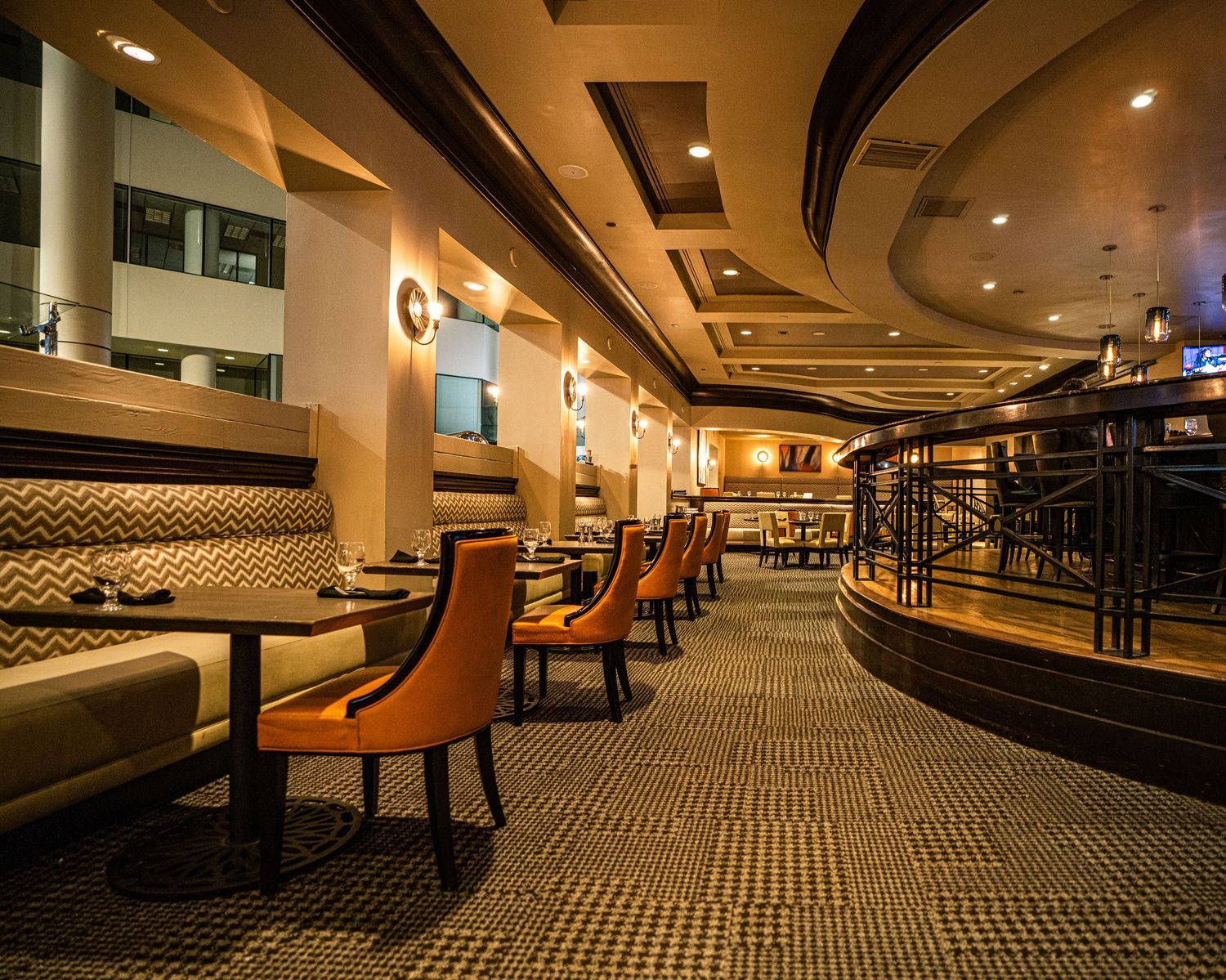 Elegant restaurant interior with orange chairs, booth seating, patterned carpet, and warm ambient lighting.
