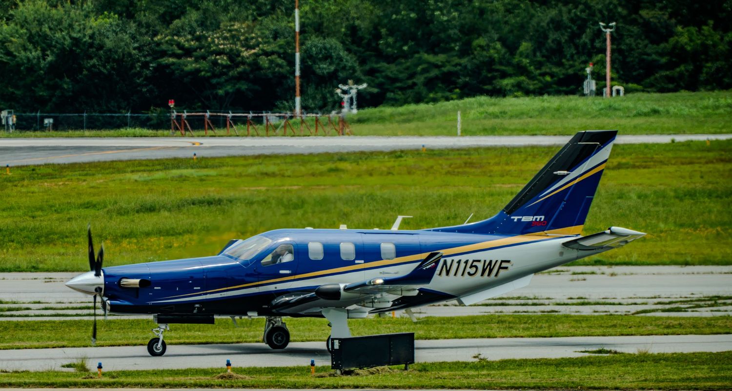 Blue and white single-engine turboprop aircraft N115WF taxiing on runway at small general aviation airport.