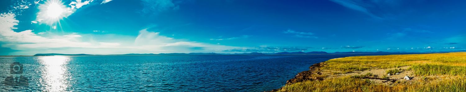 Panoramic landscape of turquoise ocean meeting yellow coastline under bright blue sky.