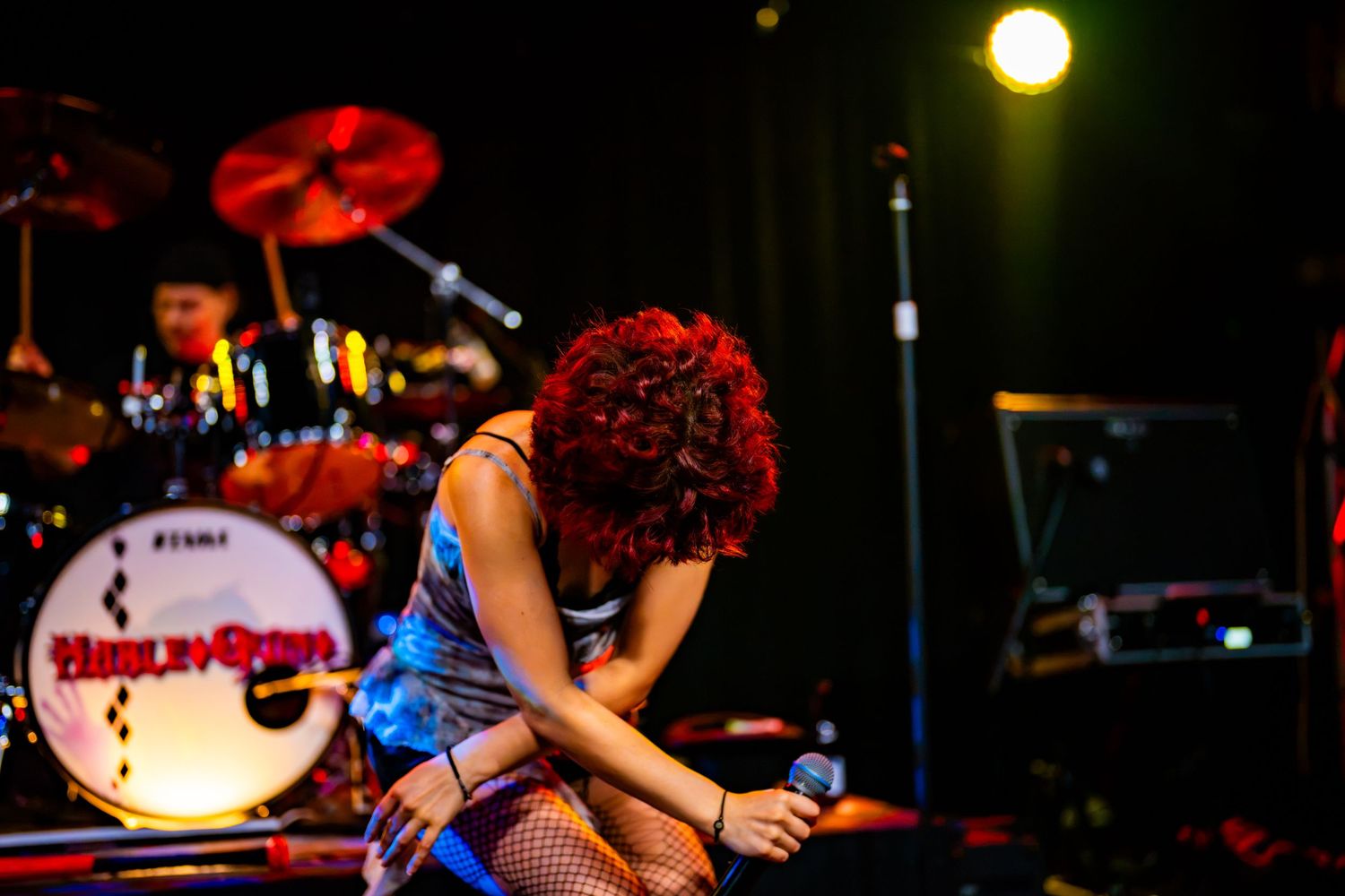 Female singer with red curly hair bowing on stage, holding microphone, with drum kit visible behind her.