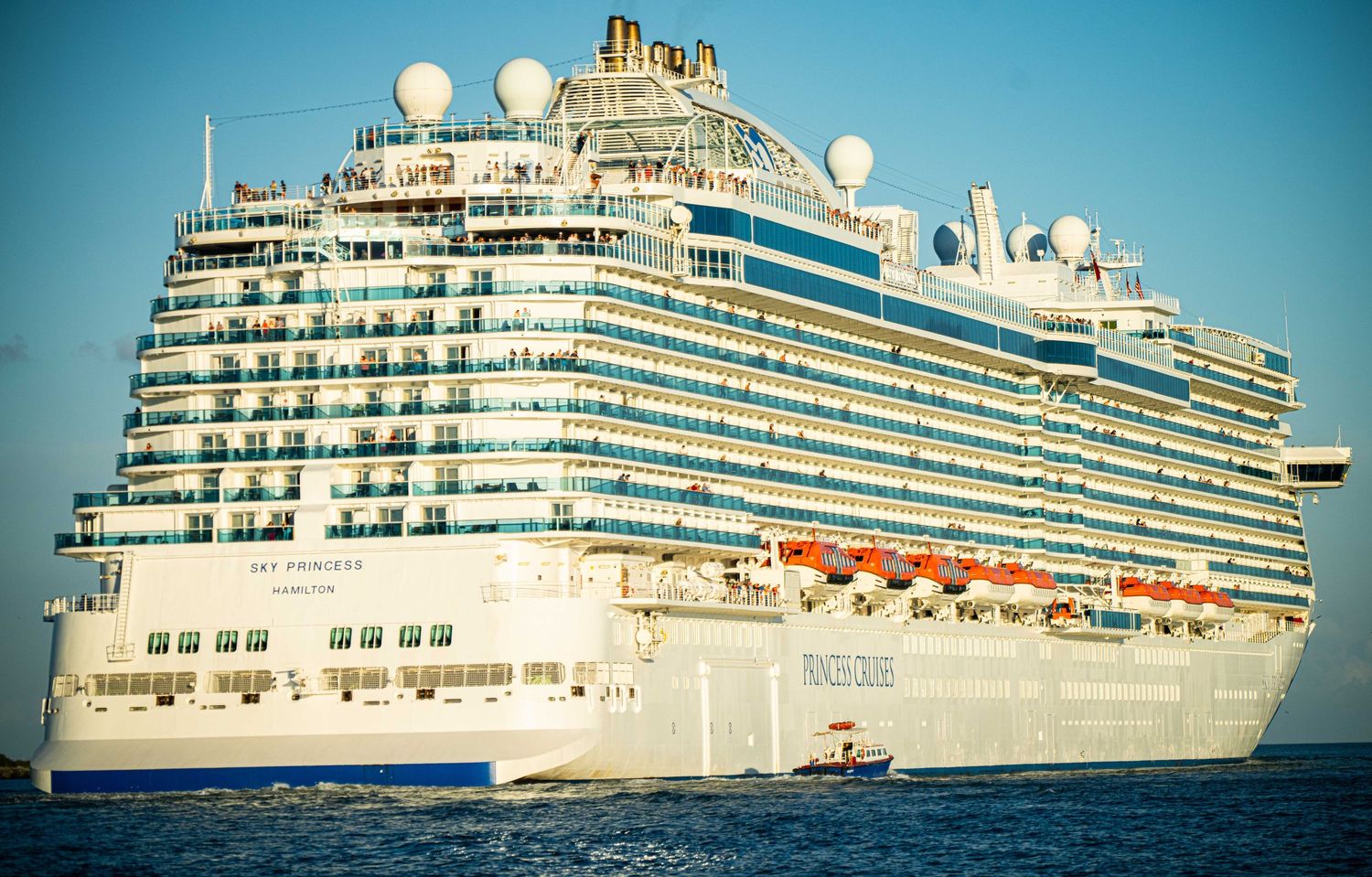 Luxury cruise ship with white exterior and multiple decks sailing across blue ocean waters under clear sky.