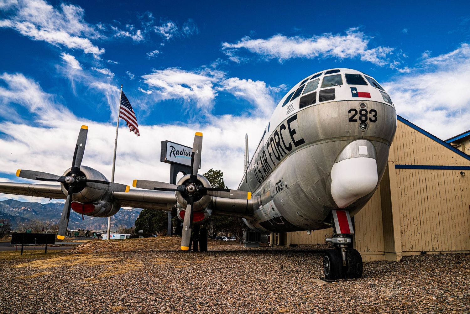 A vintage military aircraft with American flag displays against bright blue sky at an aviation museum.