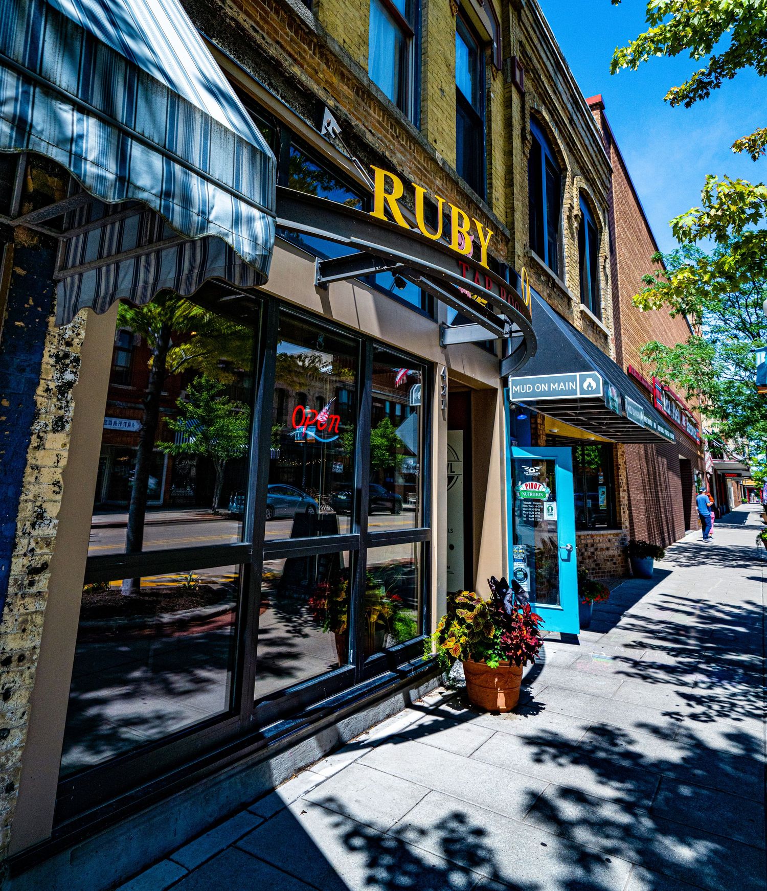Ruby storefront with large windows and awning on a sunny downtown street.