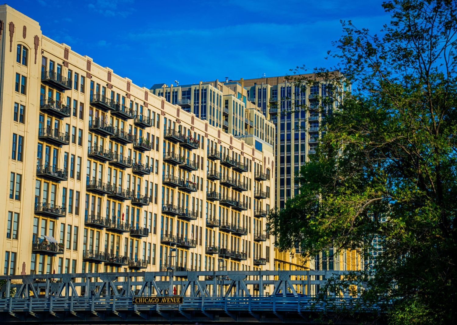 Panoramic view of a beige apartment complex with rows of balconies against bright blue sky.