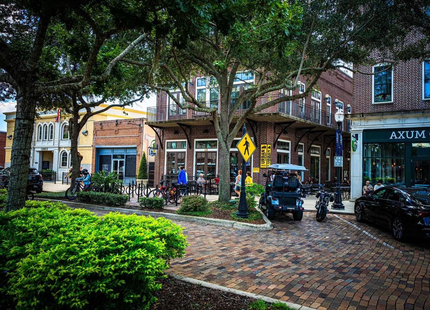 Tree-lined commercial street with brick pavers and parked vehicles in downtown area.