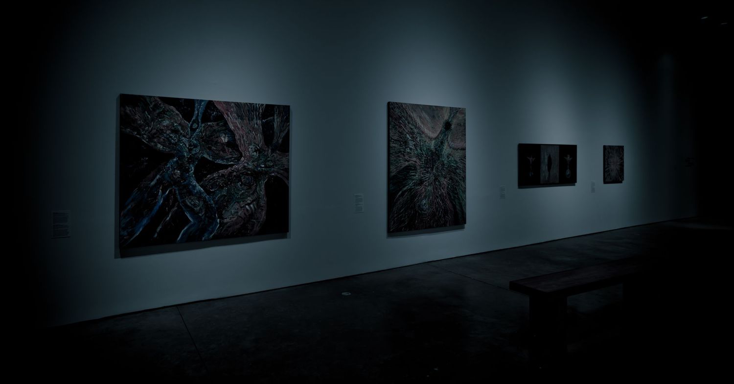 Dark gallery room displaying large abstract paintings with blue and black tones on a dimly lit wall.