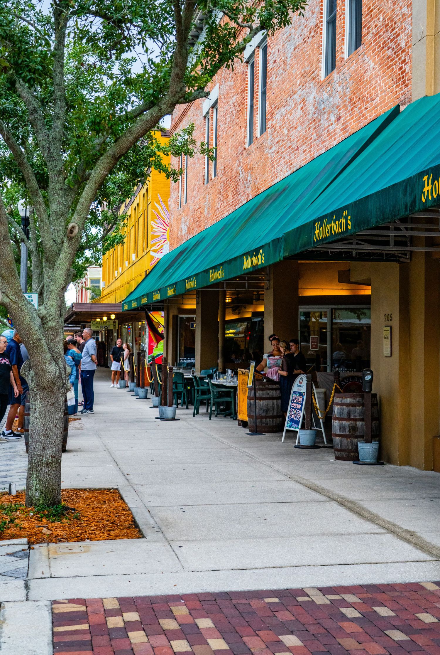 Tree-lined street with green awnings and brick buildings along a shopping district sidewalk.