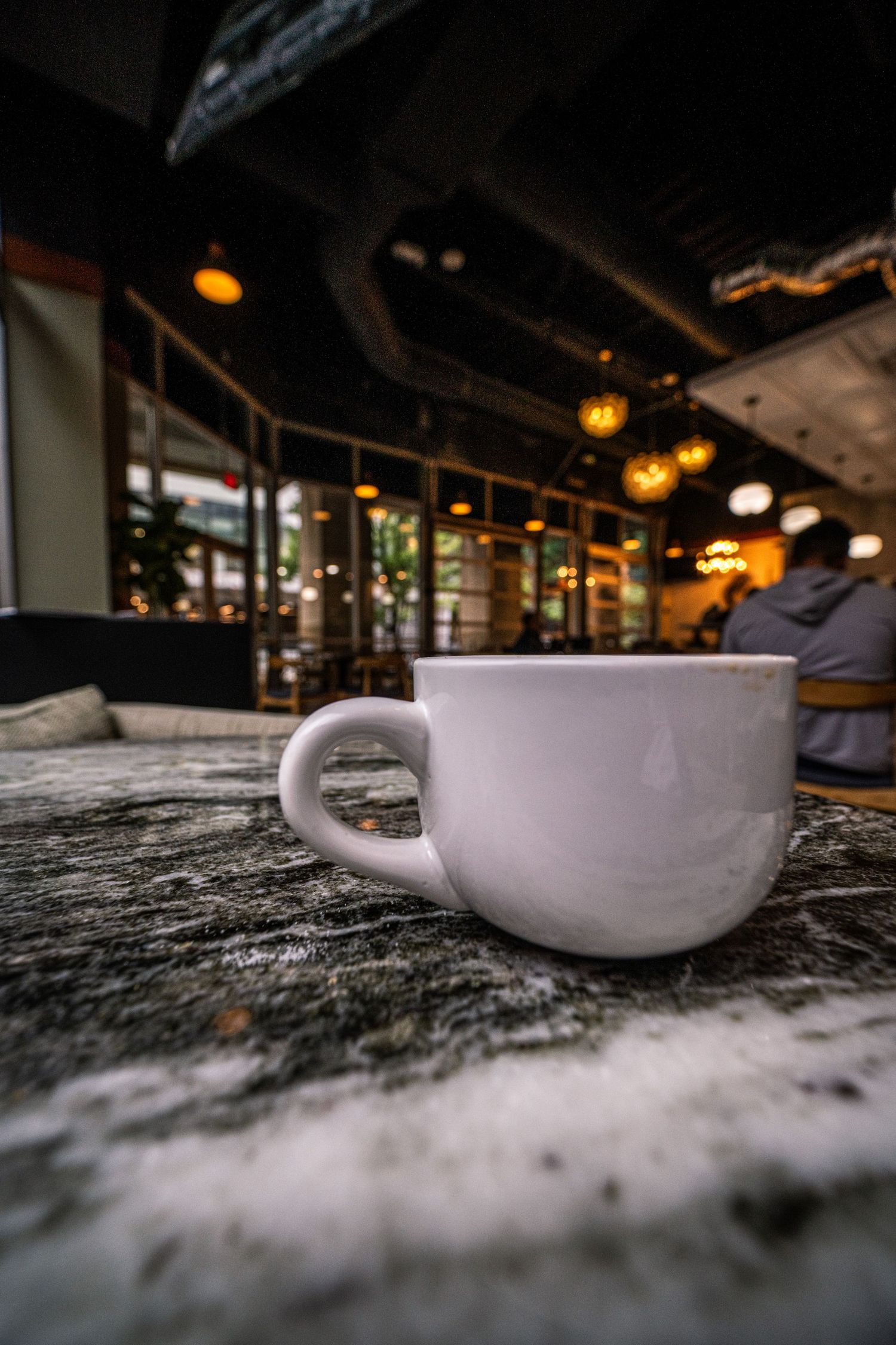 White ceramic coffee cup on textured stone surface in dimly lit restaurant interior.