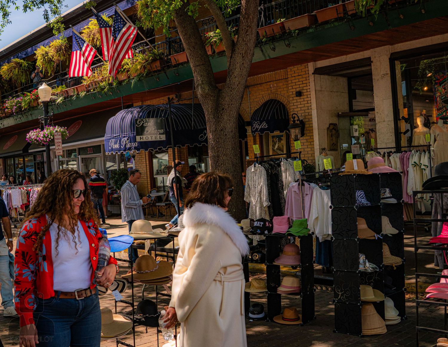 Street view of outdoor market stalls with American flags and shoppers browsing merchandise.