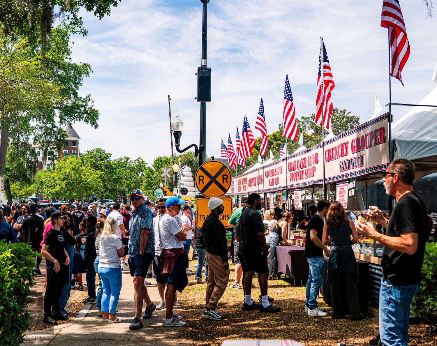 Festival attendees walking between vendor booths with American flags displayed overhead.