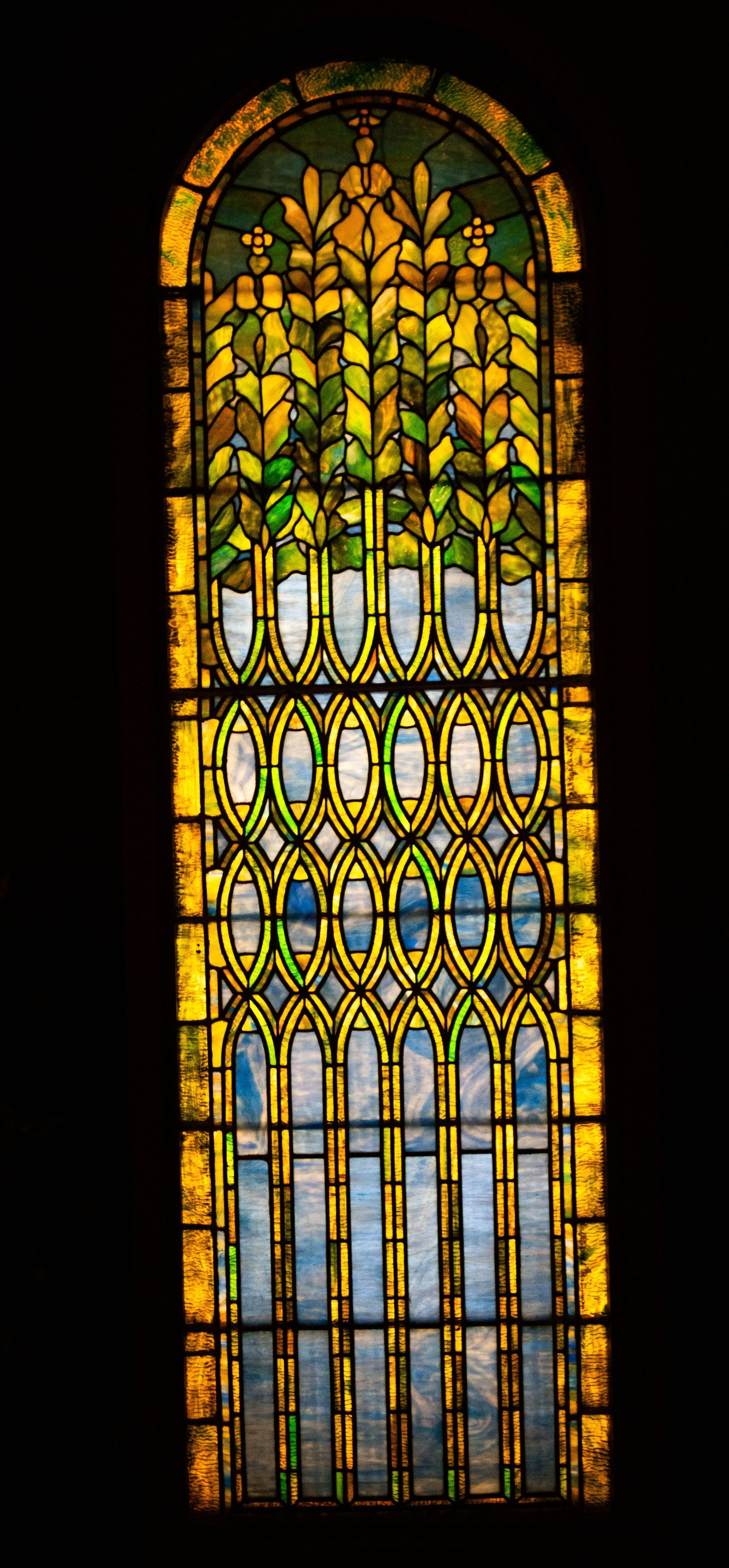 Ornate stained glass church windows with geometric patterns in yellow and green tones arranged in an arched design.