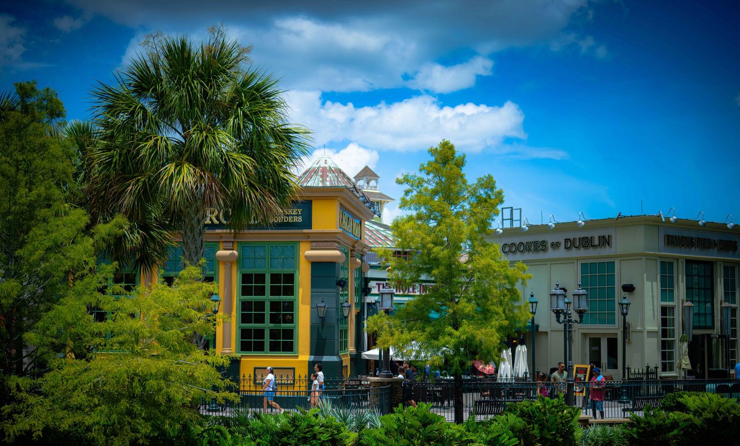 Colorful outdoor shopping plaza with palm trees, blue sky, and storefronts including Cookies of Dublin on a sunny day.