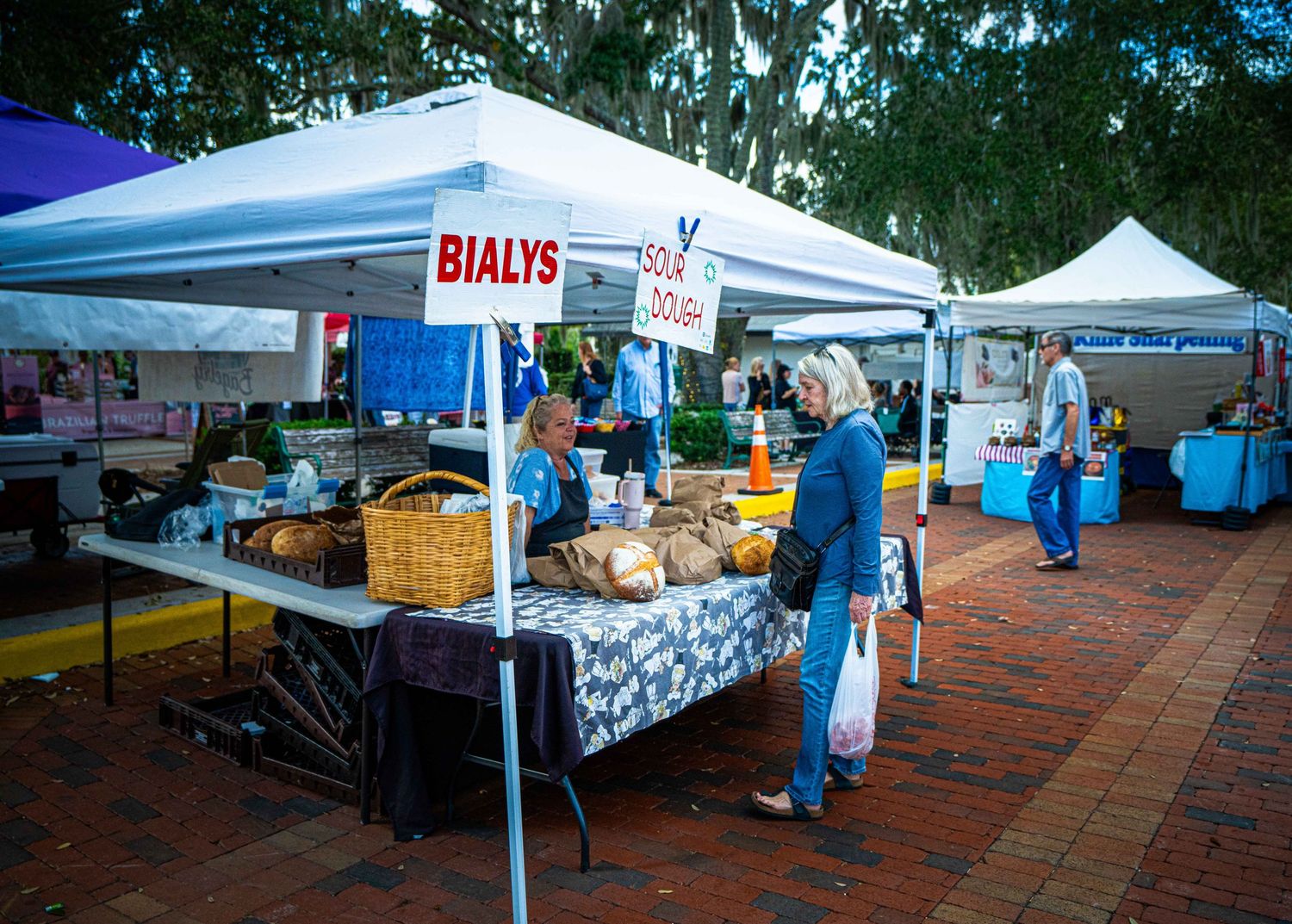 Outdoor market vendors set up white tents and display tables with merchandise at a local farmers market.