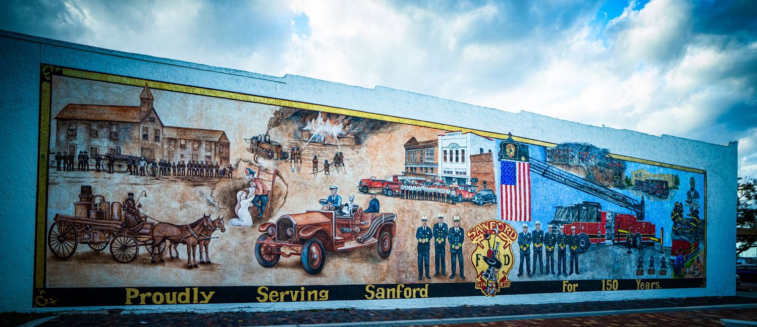 A vintage-style mural depicting historical transportation scenes with trains, horse-drawn carriages and old vehicles against a blue sky.