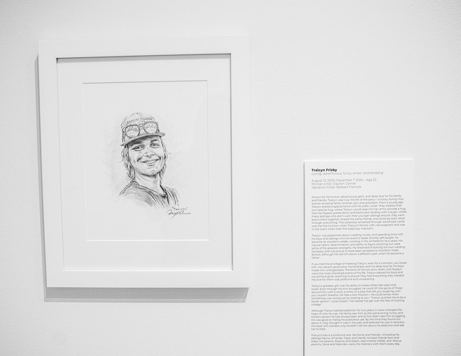 Black and white gallery wall displaying portrait sketches and text descriptions about drug addiction stories.