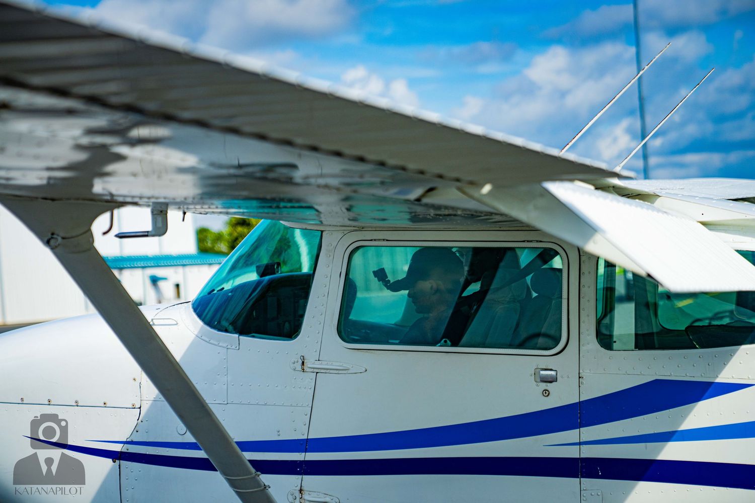 Side view of a small aircraft cockpit showing windows and white exterior with blue striping.