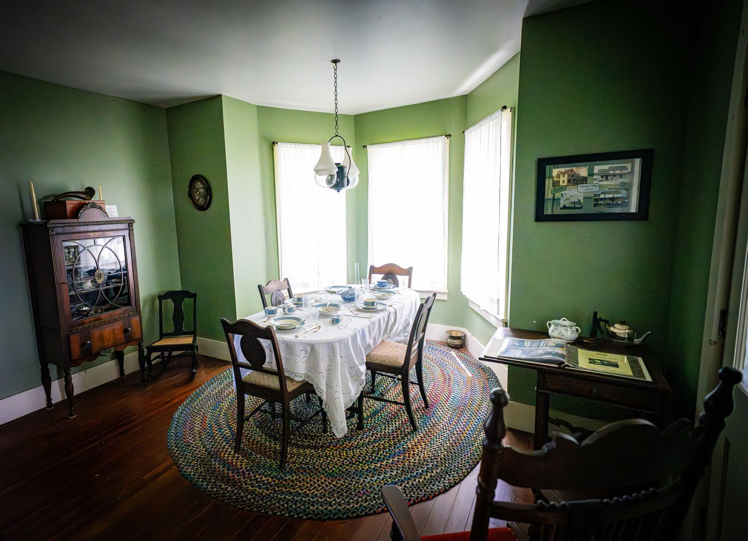 Victorian dining room with green walls, round table, and bay windows decorated in period style.
