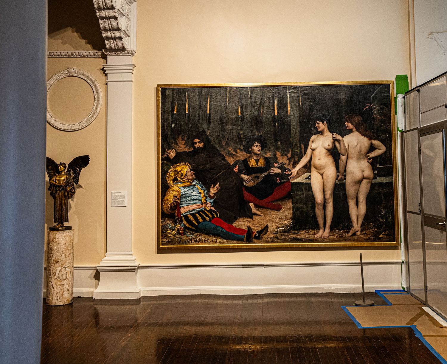 Classical art gallery interior displaying multiple paintings and sculptures in ornate gold frames.