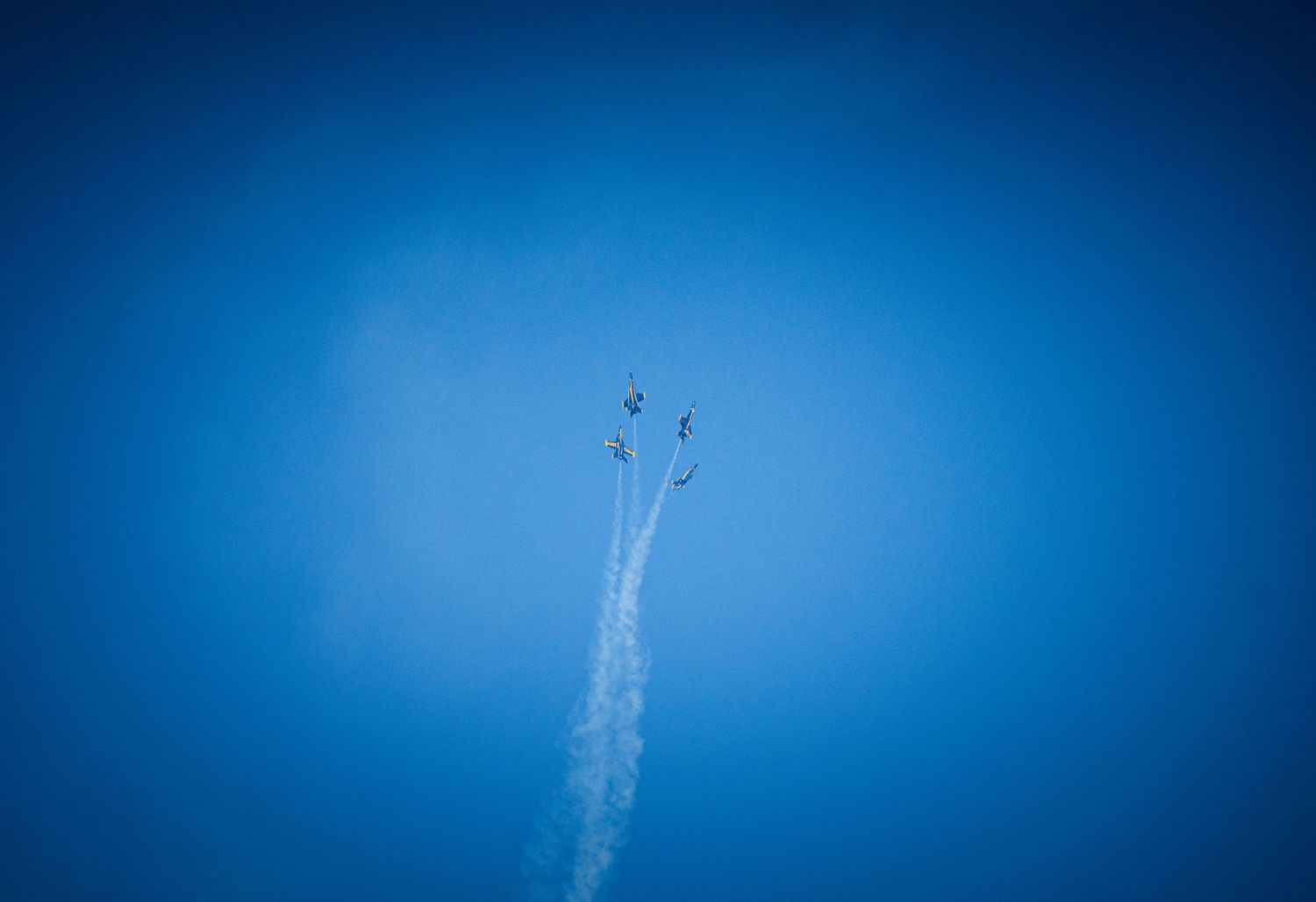 Jets flying in formation against bright blue sky with white contrails trailing behind.