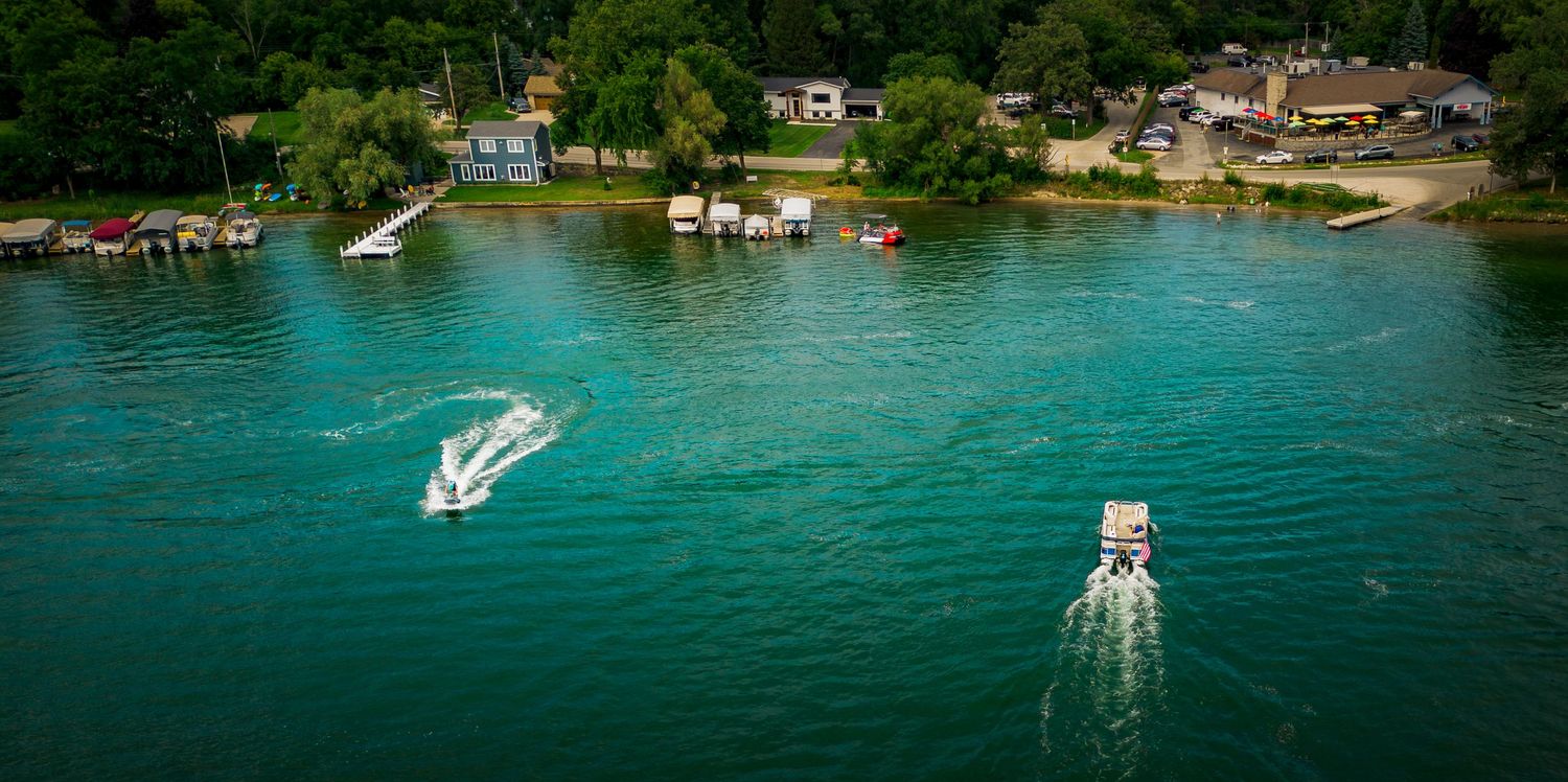 Aerial view of waterfront homes and docks along a turquoise lake with boats.