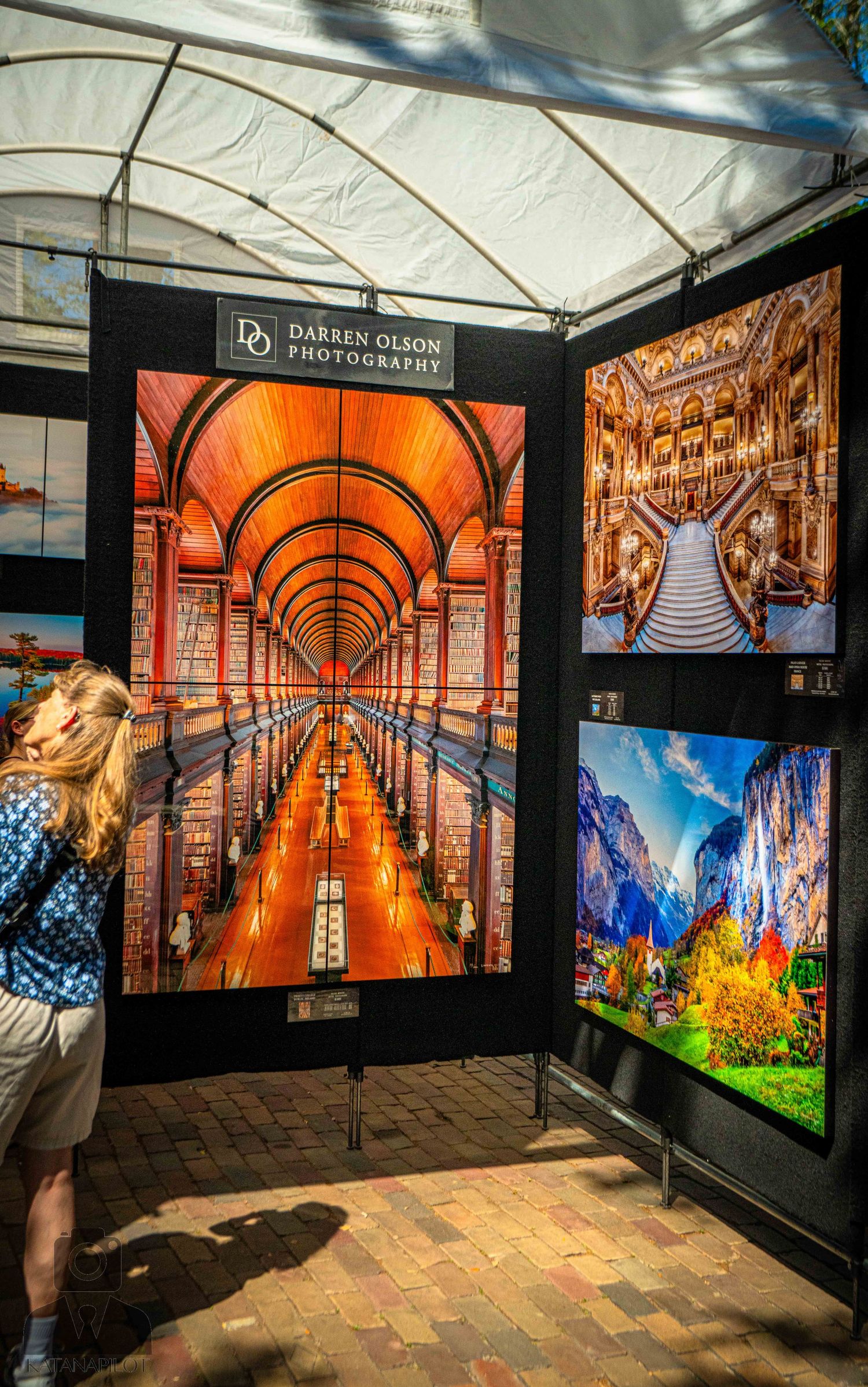 Art exhibition display featuring vibrant photographs including an illuminated orange tunnel and ornate architectural scenes.