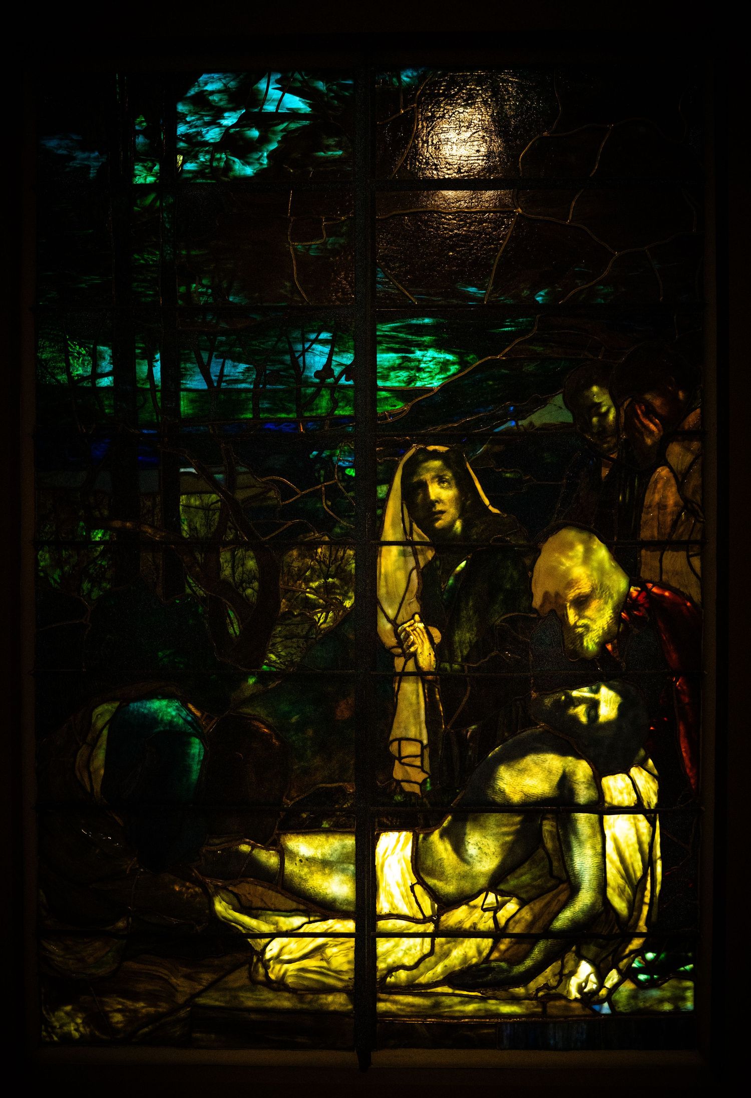 Stained glass panel depicting a religious scene illuminated with dramatic yellow and green lighting.