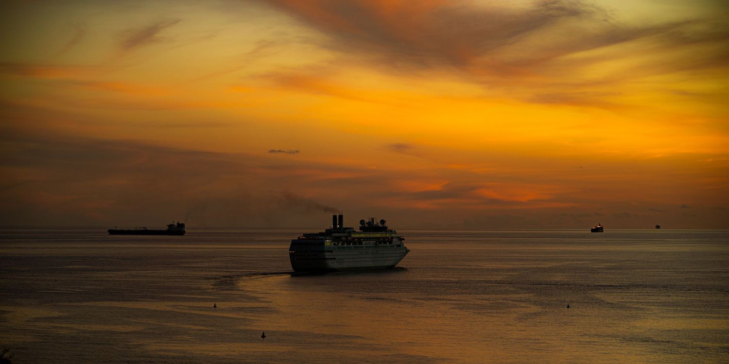 Silhouette of ships on horizon during dramatic orange sunset over ocean.