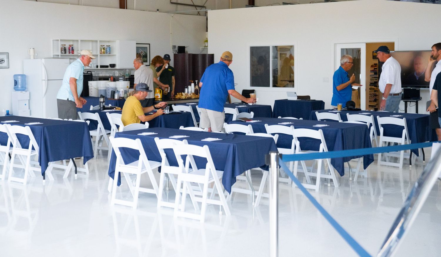 People seated in white folding chairs in a large industrial space with exposed ceiling and white walls.