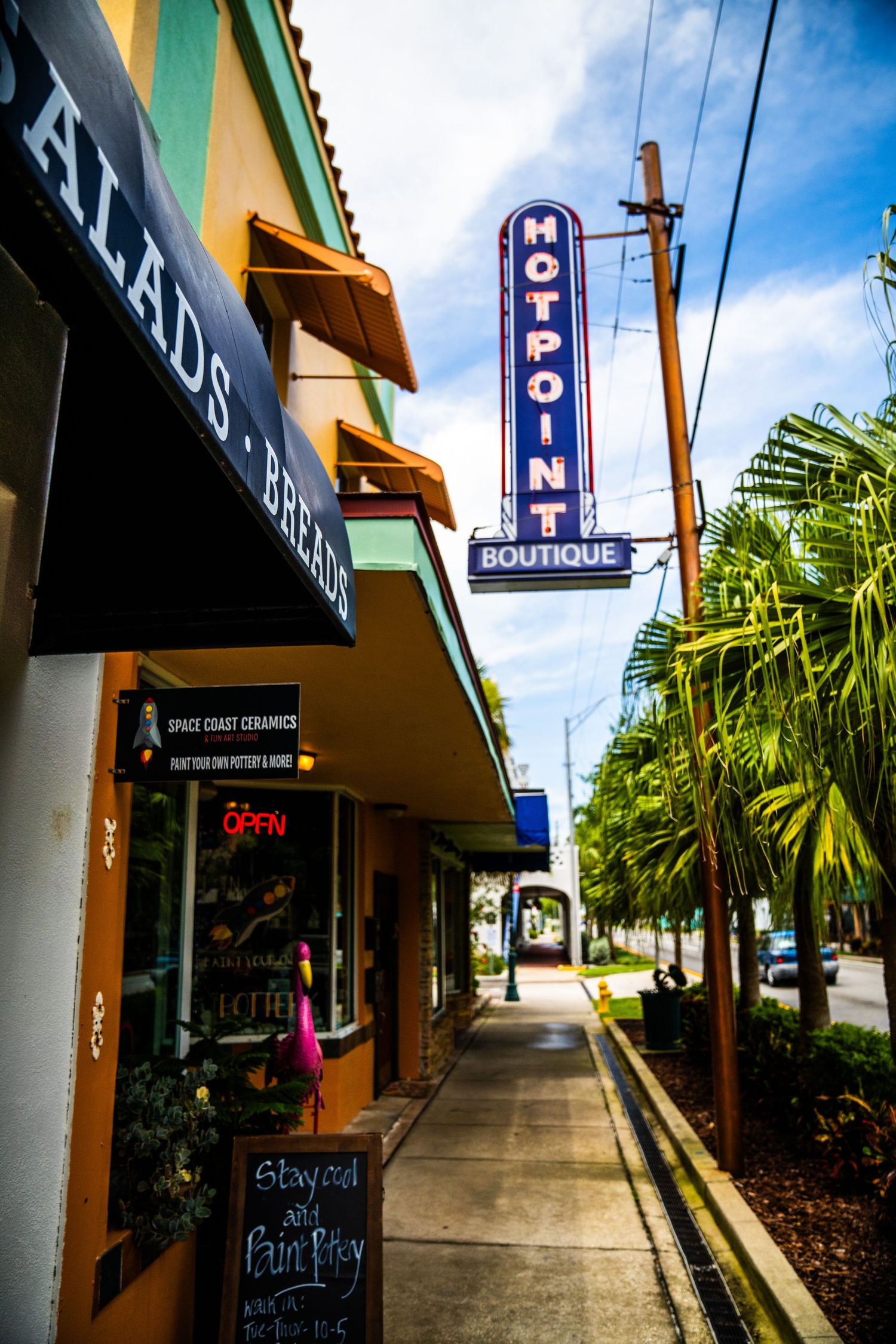 Urban sidewalk with blue neon signs and palm trees along a commercial strip.
