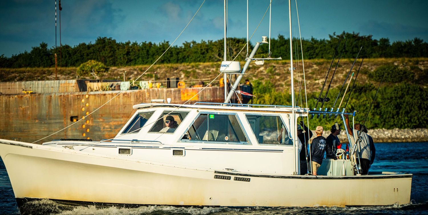 Row of fishing boats docked at a marina with trees and buildings in the background on a sunny day.