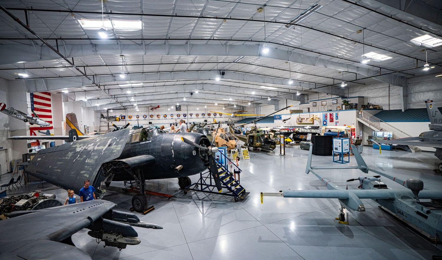 Military aircraft on display inside a spacious aviation museum hangar with American flags and exhibits.