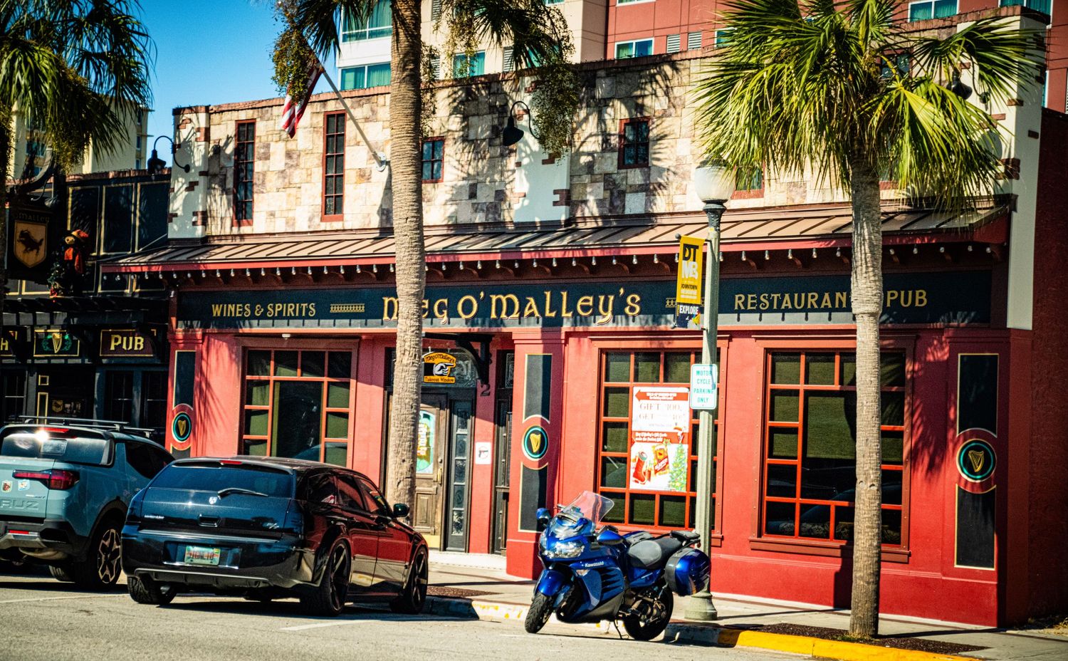 Colorful street view of historic buildings with palm trees and parked cars along a tropical downtown area.