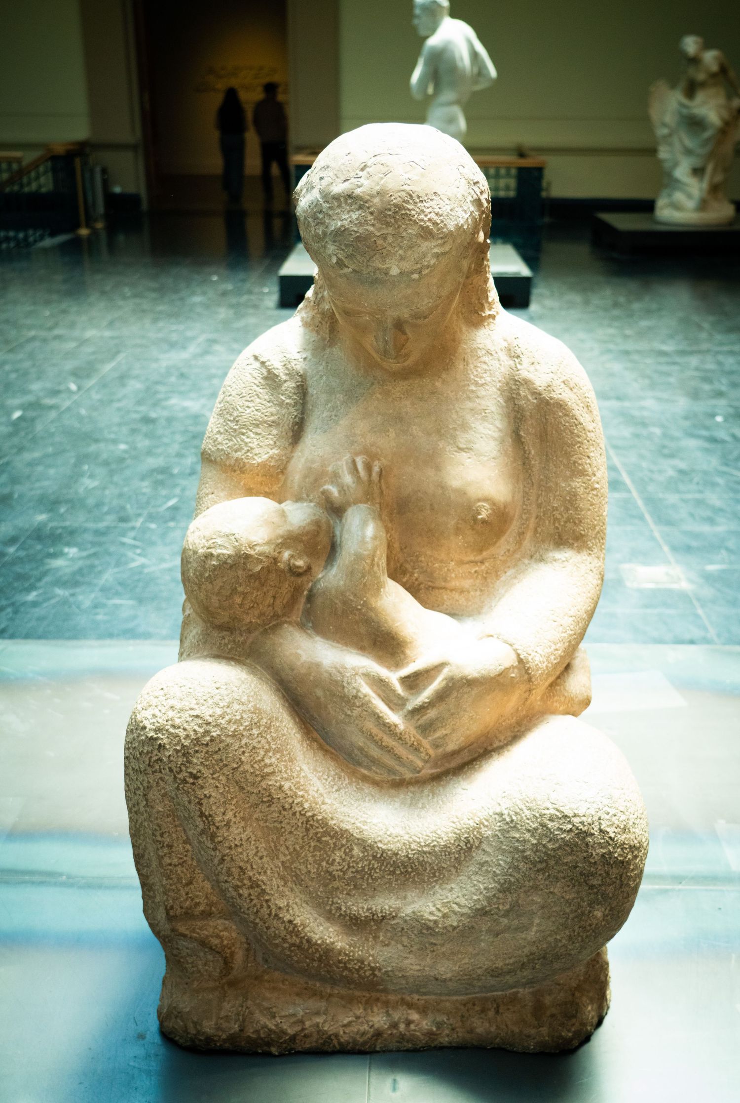Ancient stone sculpture of a seated figure displayed in museum setting.