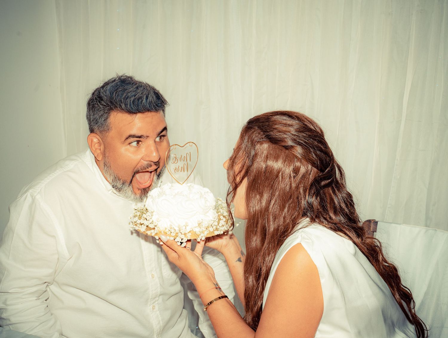 A couple shares a romantic moment during their wedding photo session against a white backdrop.
