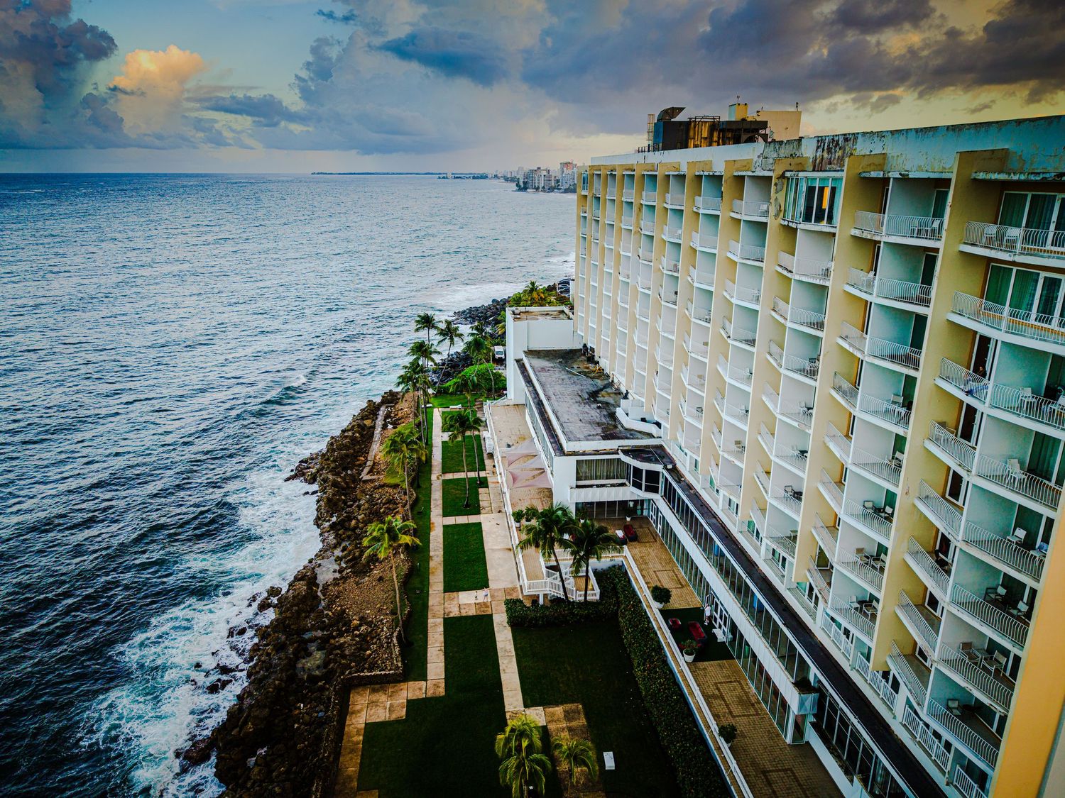 Luxury oceanfront resort buildings with balconies perched dramatically on cliffs above the Pacific Ocean in Hawaii.
