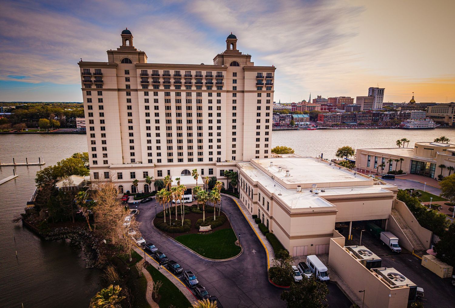 Luxury waterfront hotel in Savannah Georgia with curved driveway and dramatic sunset sky over the river.
