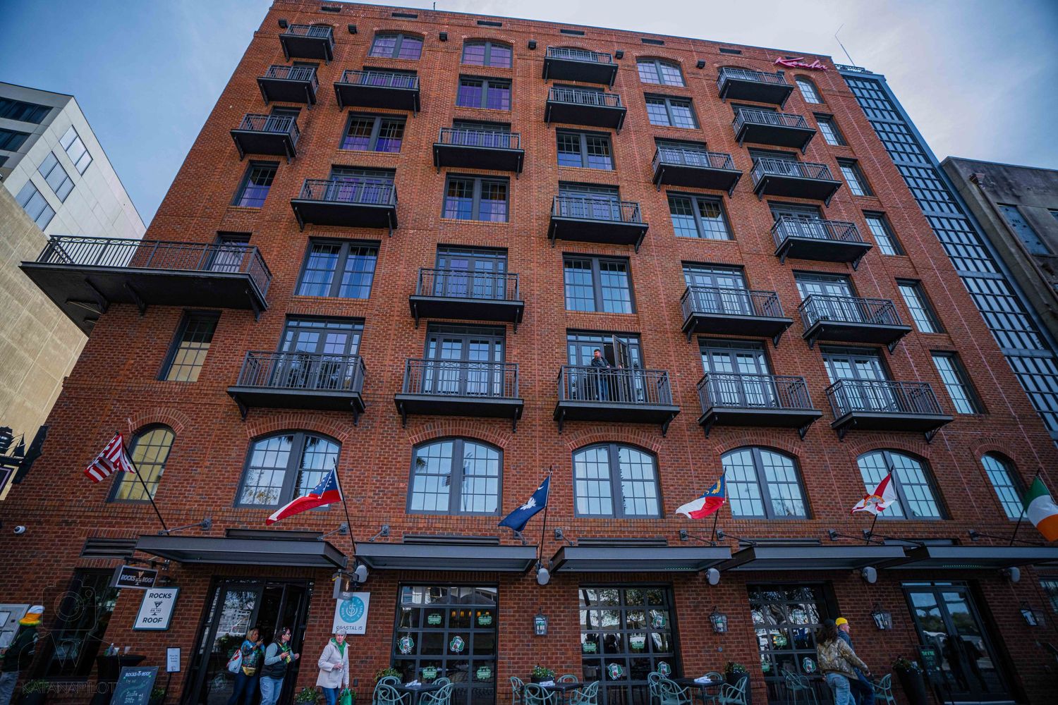 Historic red brick apartment buildings with fire escapes line an urban street against a blue sky.