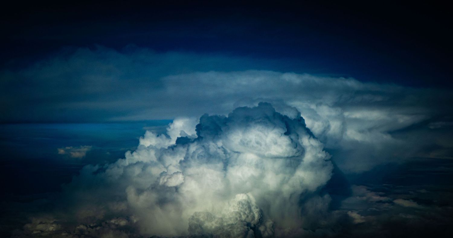 Dramatic aerial view of massive cumulonimbus storm clouds billowing against a dark blue sky.