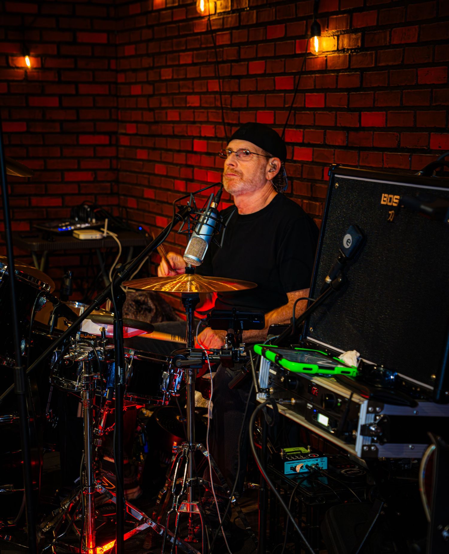 Drummer performs with electronic drum kit against red brick wall background.