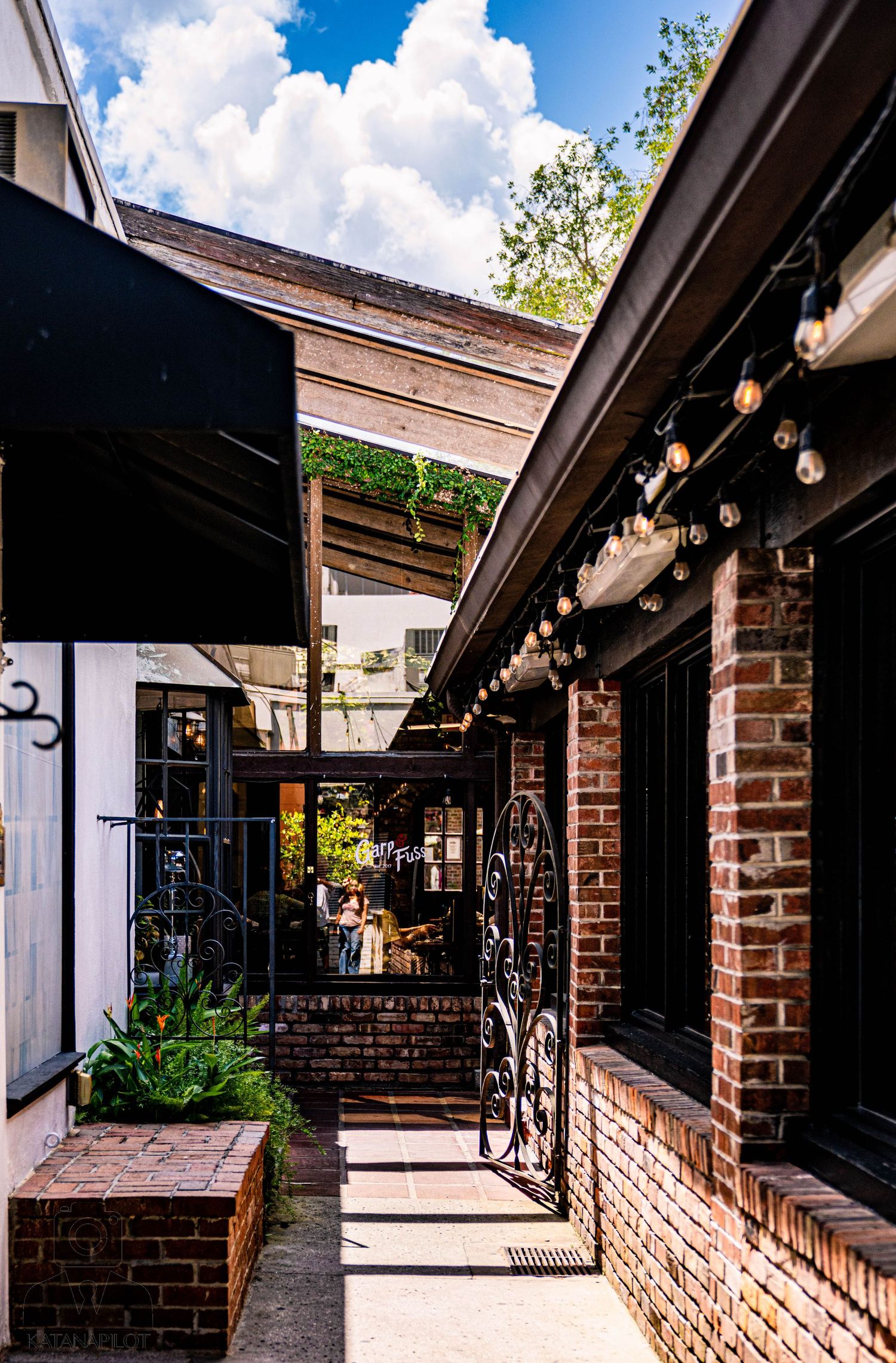 Covered brick walkway with string lights and white columns creating an architectural corridor.