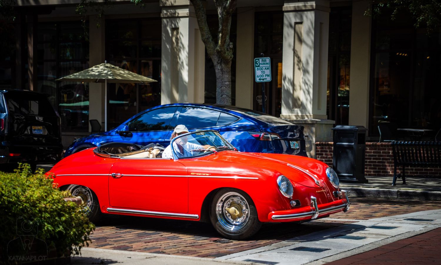 Classic red vintage sports cars are displayed on a brick paved street near storefronts.