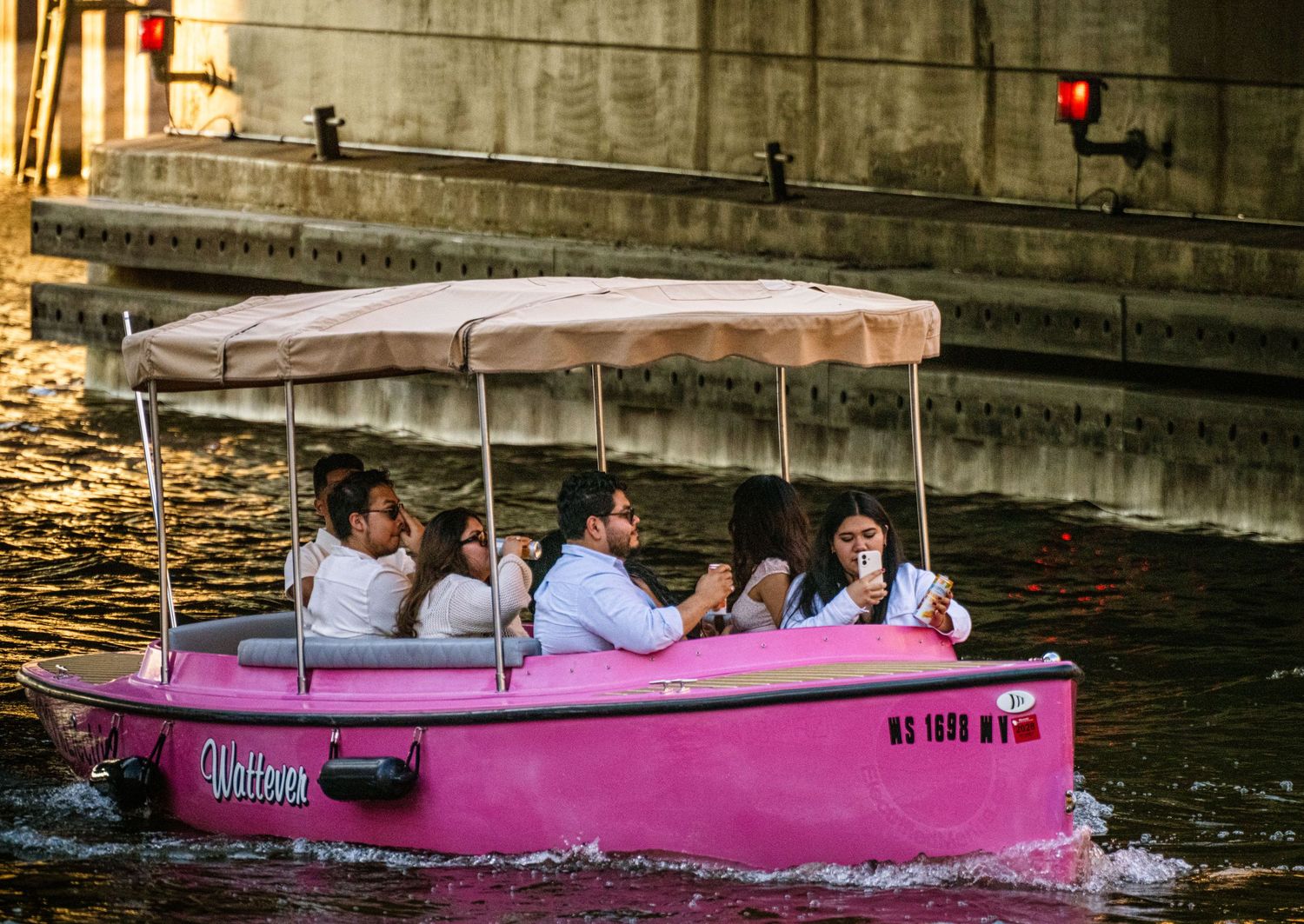 Pink and white pontoon boats cruising along an urban waterway.
