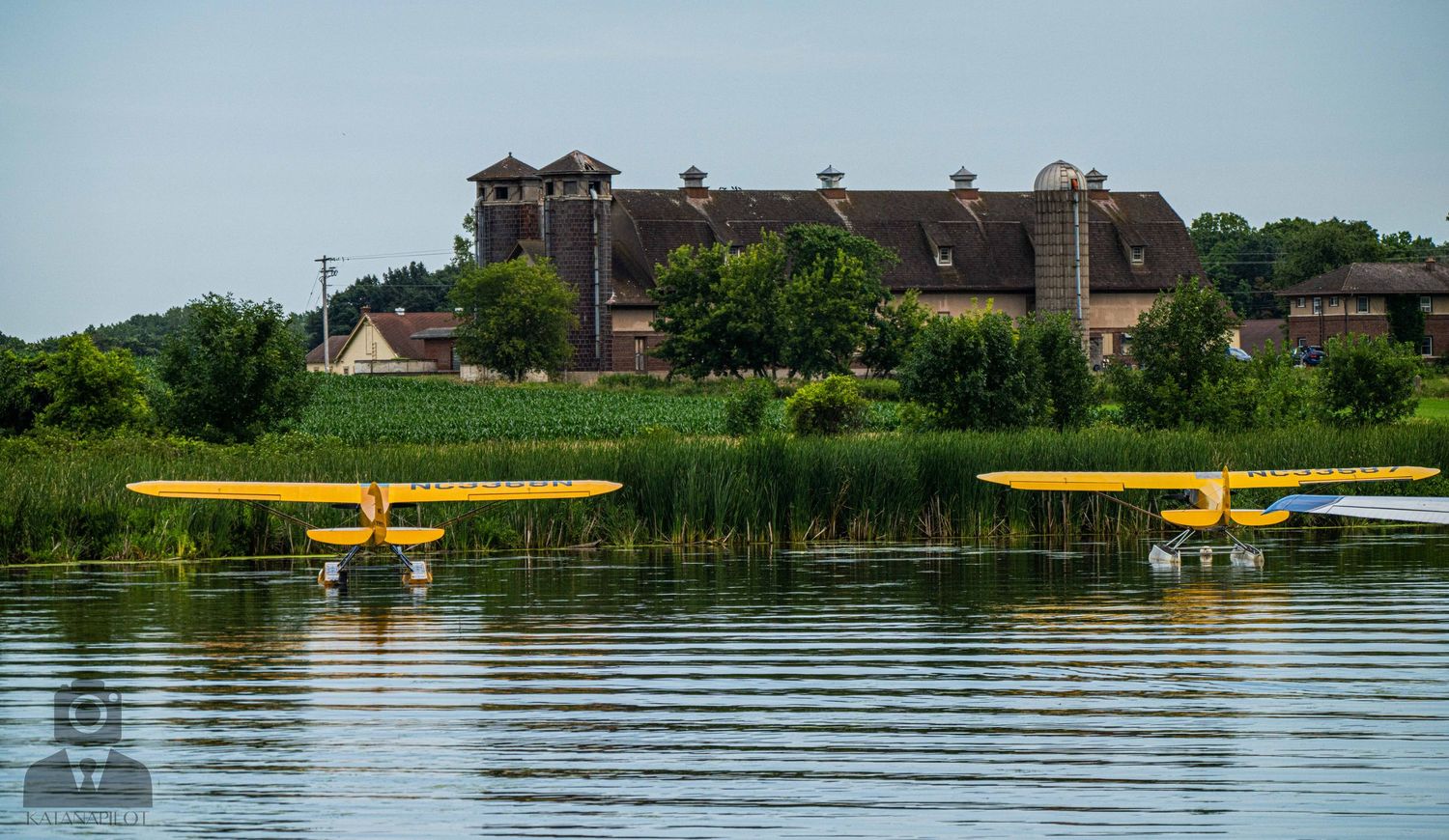 Two yellow seaplanes float on calm waters near a large building with distinctive towers.
